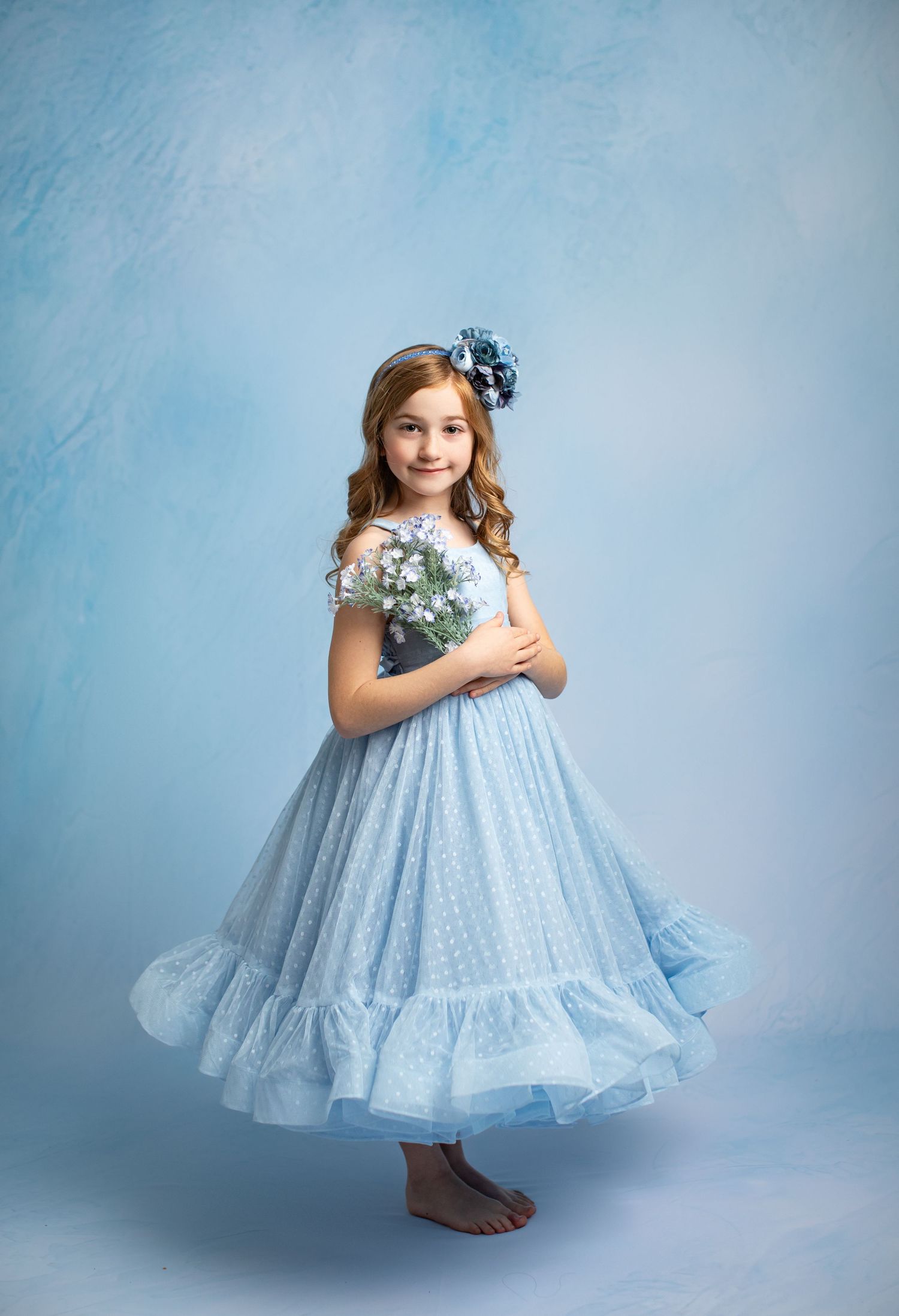 A young dancer in a navy blue tulle dress performs barefoot against a moody blue backdrop.
