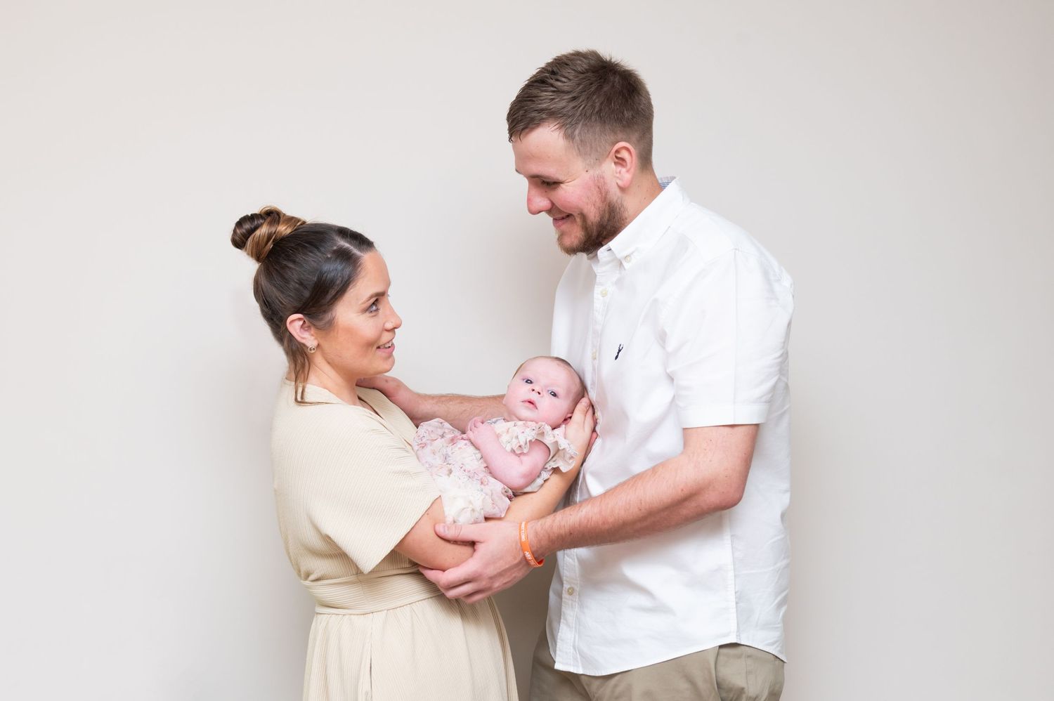 Intimate lifestyle newborn photography session with parents in neutral studio setting.