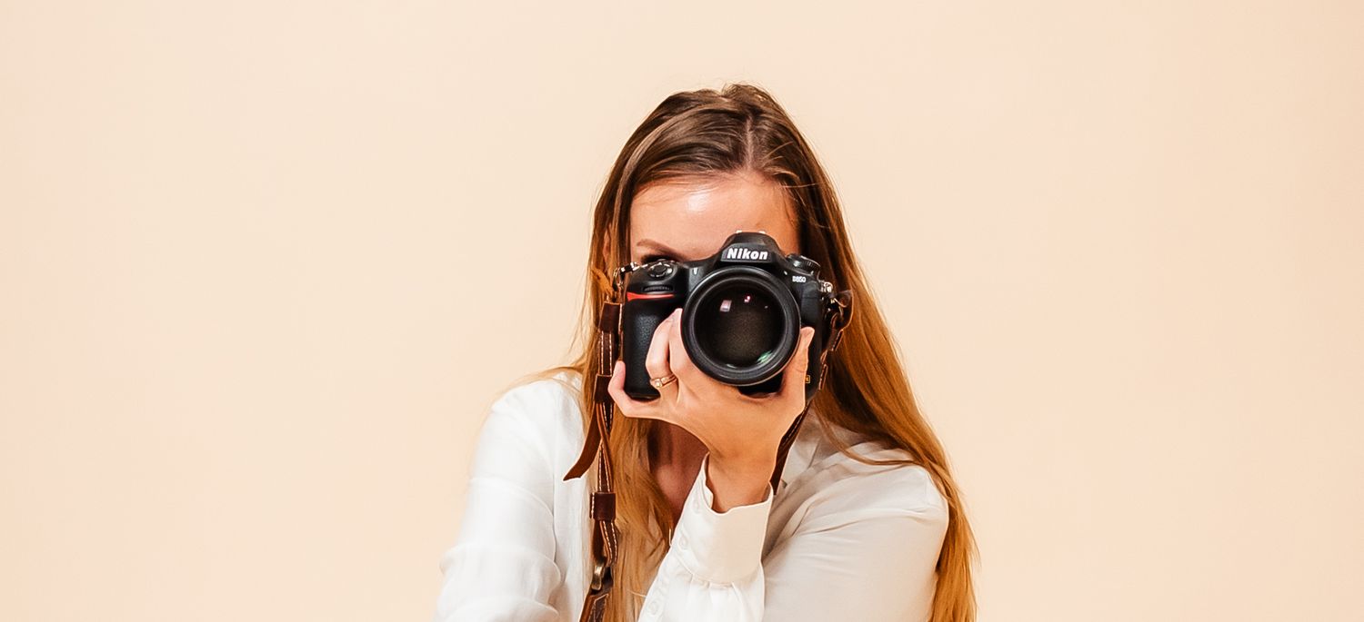 Person holding professional camera against peach colored background.