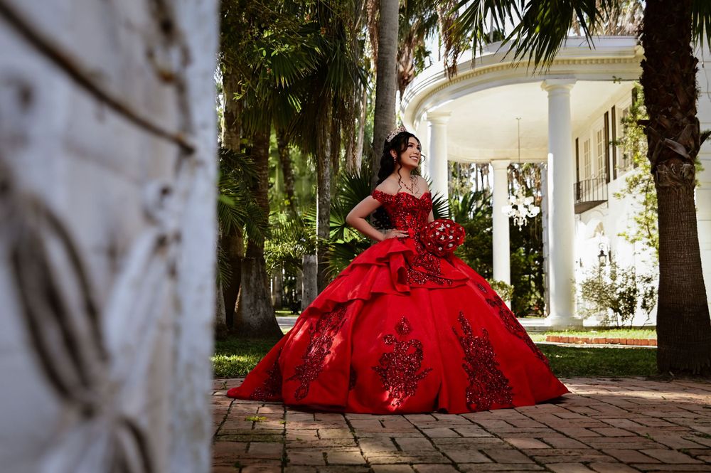 A magnificent red quinceañera dress photographed in front of a white columned mansion.