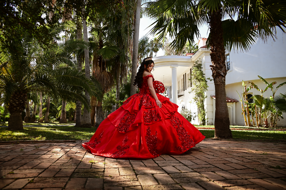 A vibrant red ball gown photographed on a brick pathway surrounded by palm trees.