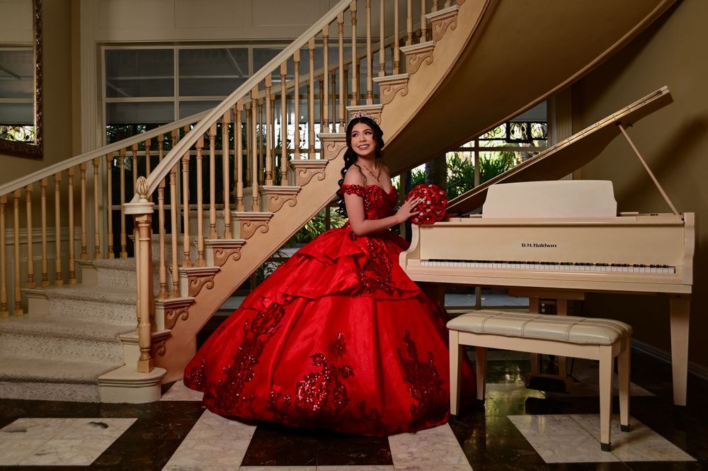 A dramatic red ball gown photographed next to a white piano in an elegant interior setting.