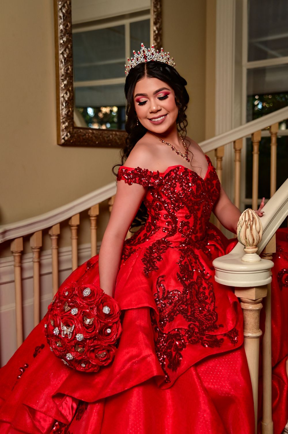 A sparkling red ball gown photographed on an elegant staircase with ornate white railings.