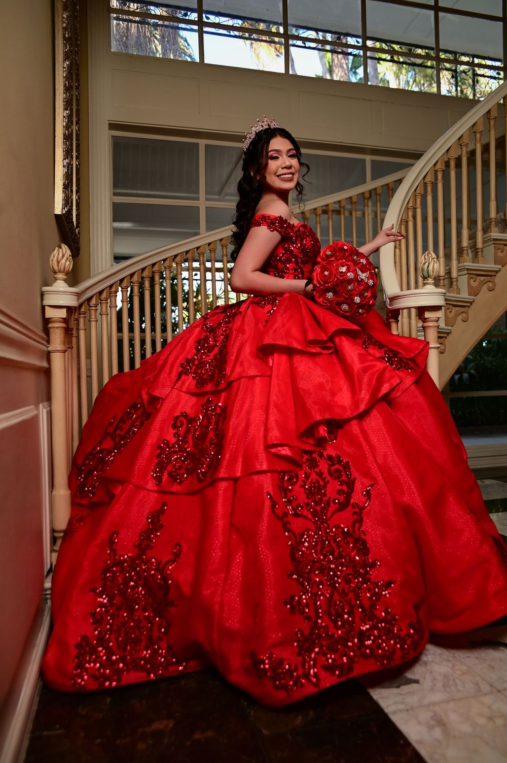 A elaborate red quinceañera gown with crystal details captured on a classic staircase.