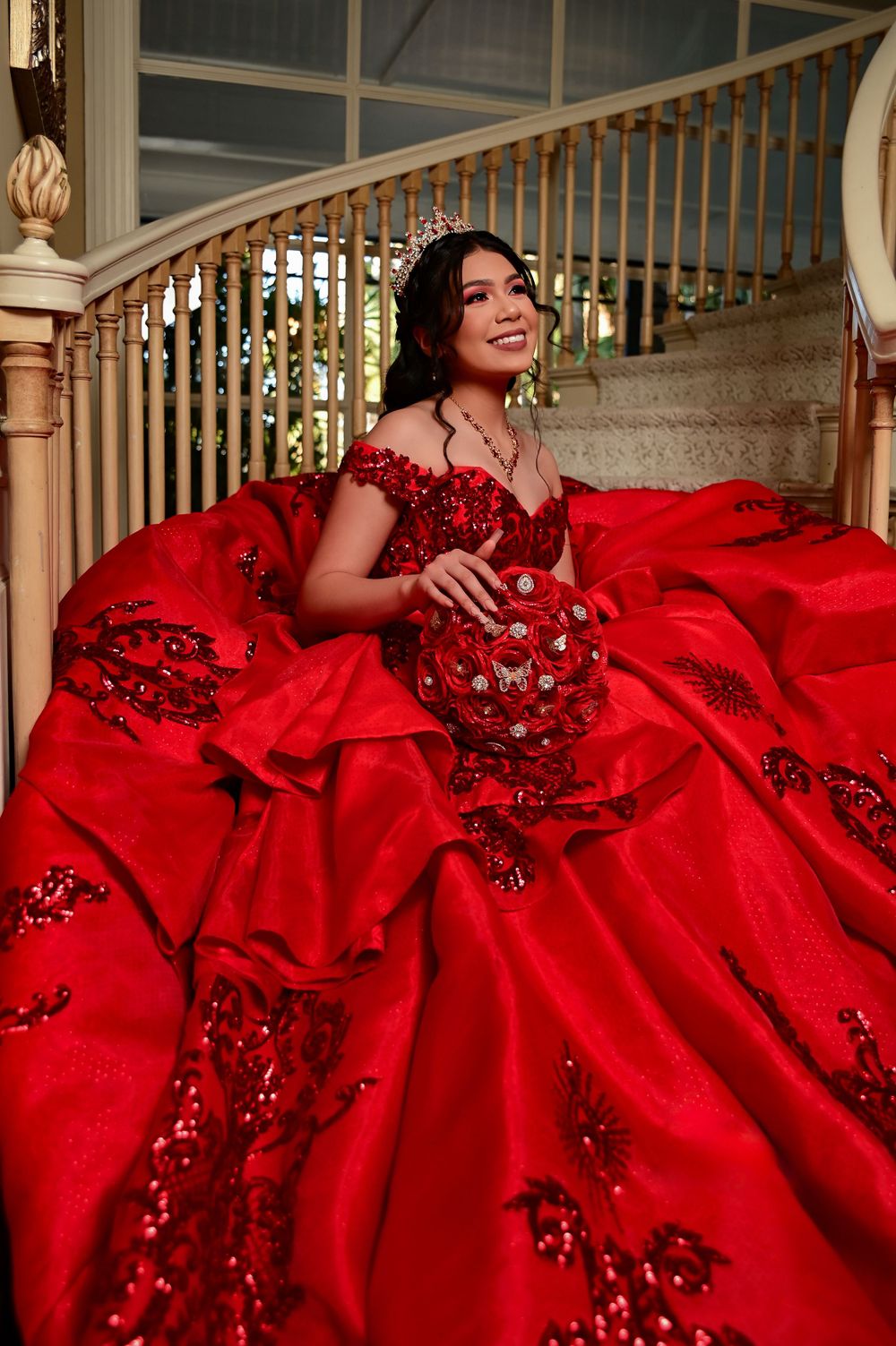 A luxurious red ball gown with crystal embellishments photographed on an elegant staircase.