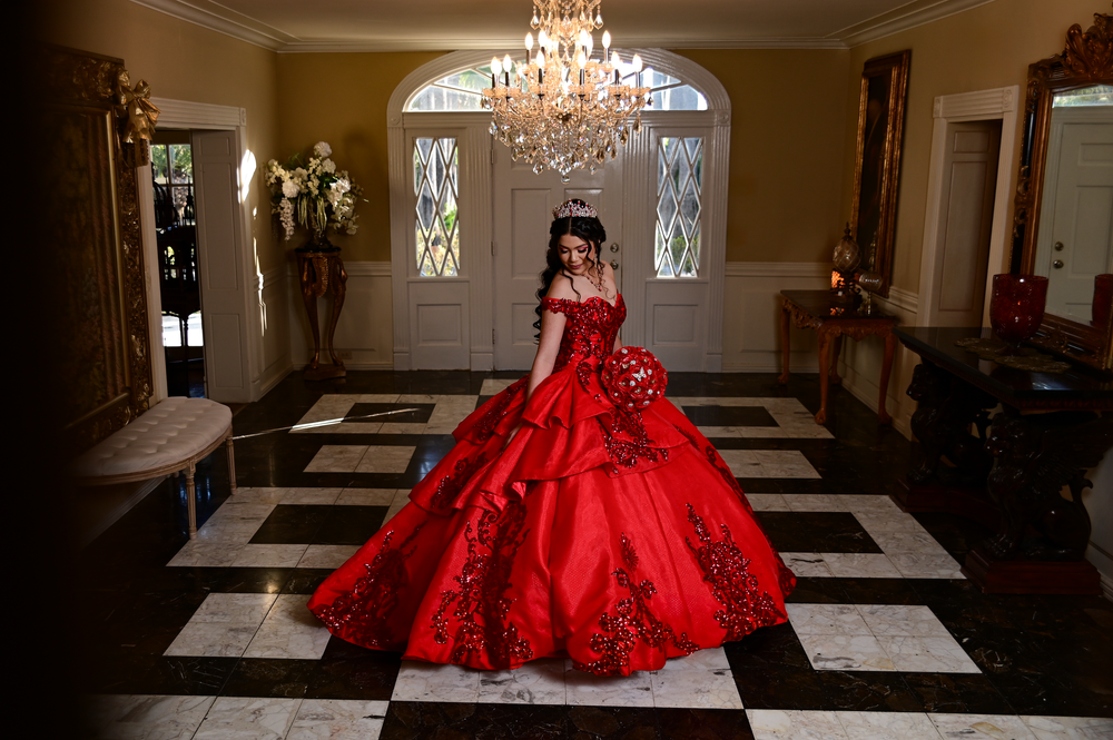 Dramatic photo of a red ball gown on a black and white checkered floor beneath a crystal chandelier.