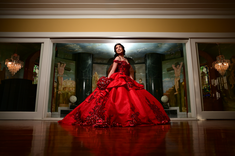 A stunning red ball gown with ornate details photographed in an elegant room with chandeliers.