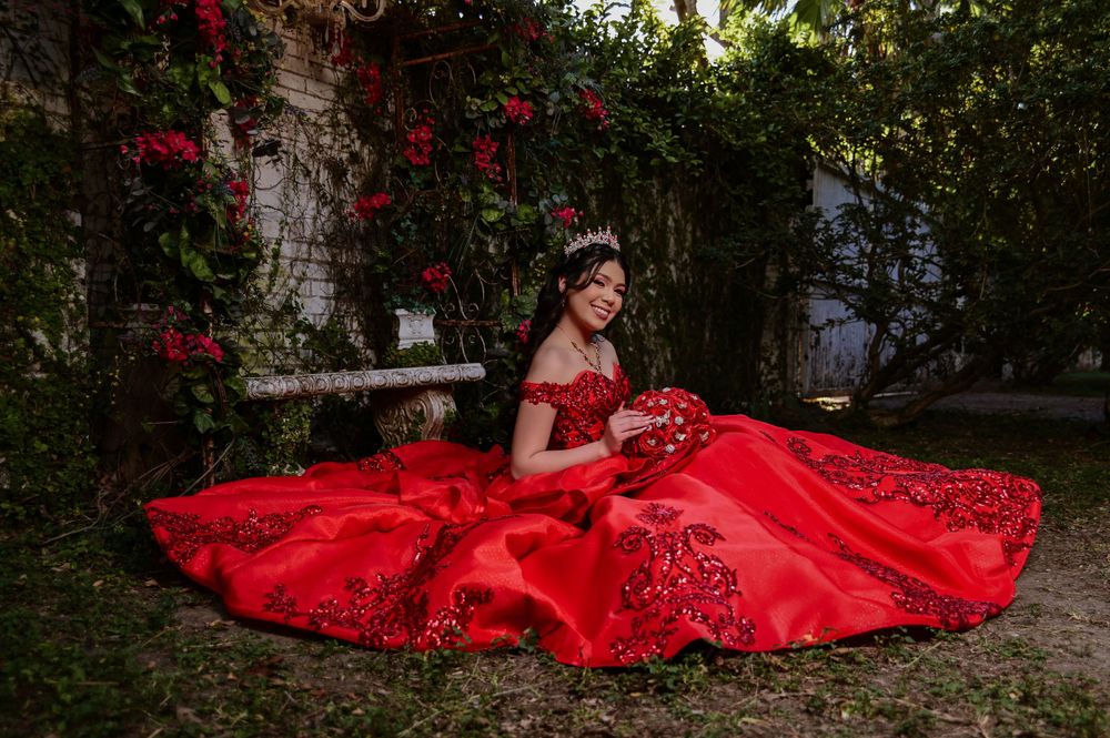Elegant red ball gown spread out in a garden setting surrounded by blooming roses.