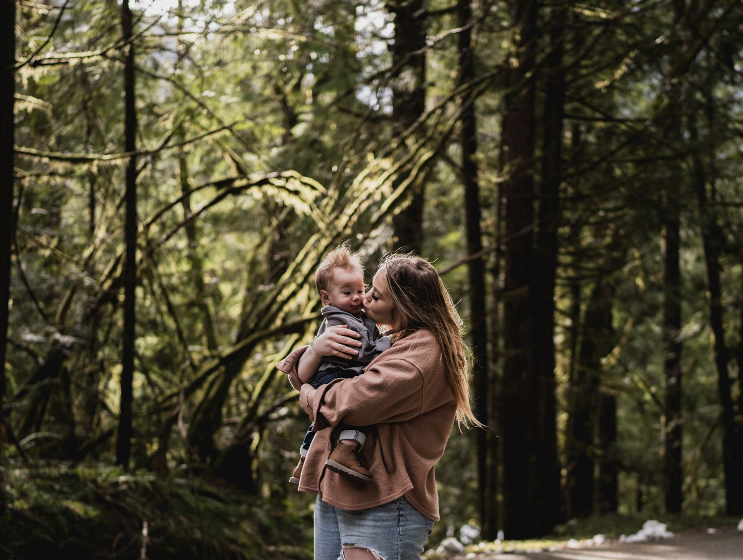 Parent and child share tender moment while exploring a misty forest trail.