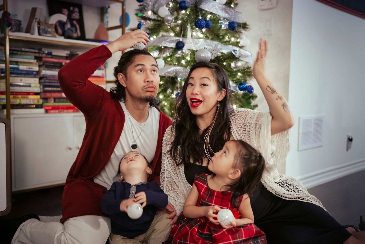 Christmas Cart photoshoot of family sitting infront of Christmas tree. Mom, Dad, daughter and son posing in a silly manor.