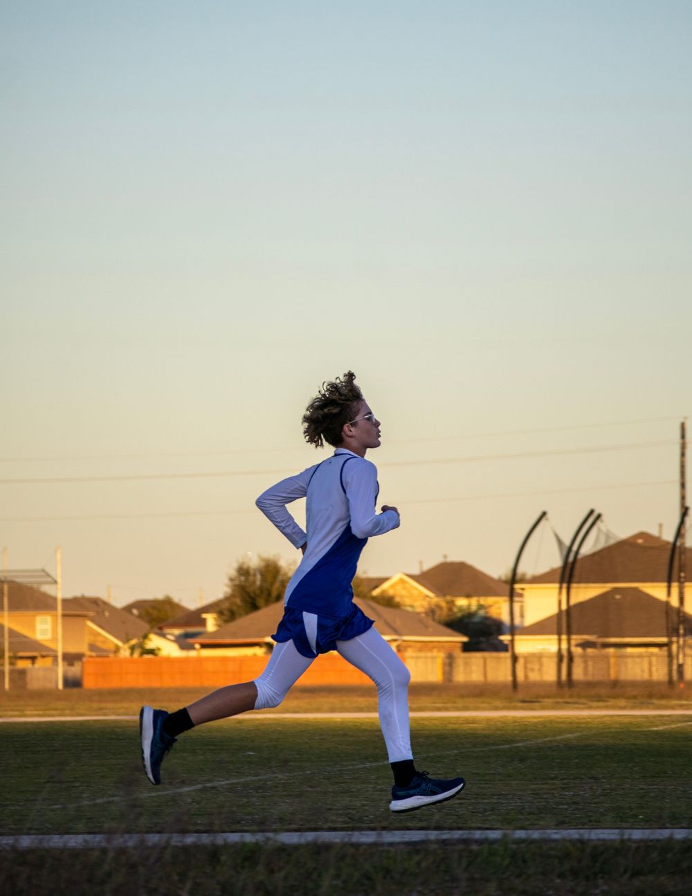 Athlete in blue uniform runs across field during sunset training session.