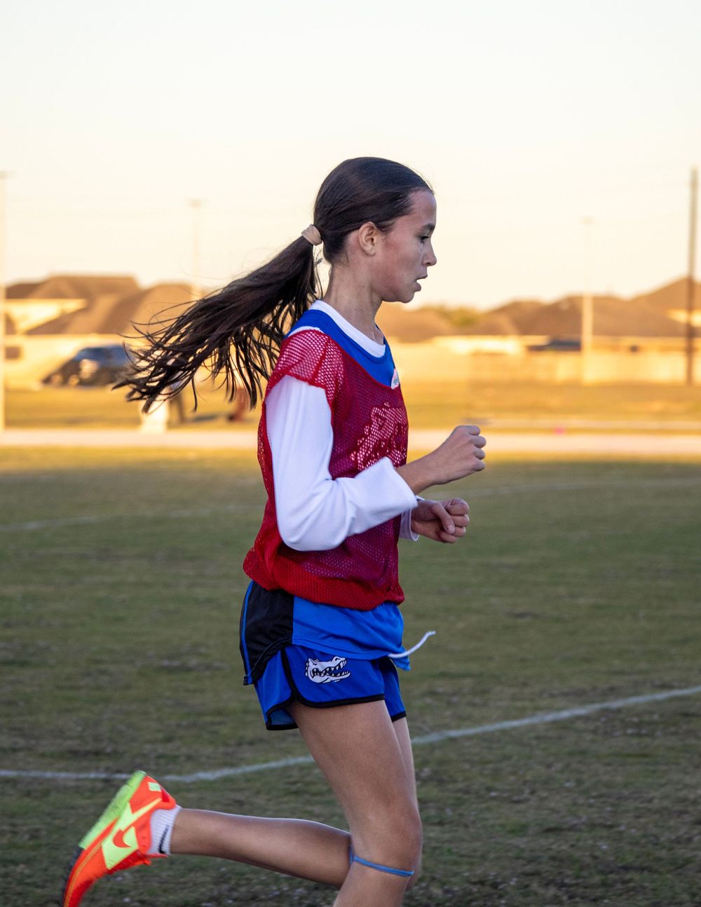 Runner in red and white uniform sprinting across an outdoor field at sunset.