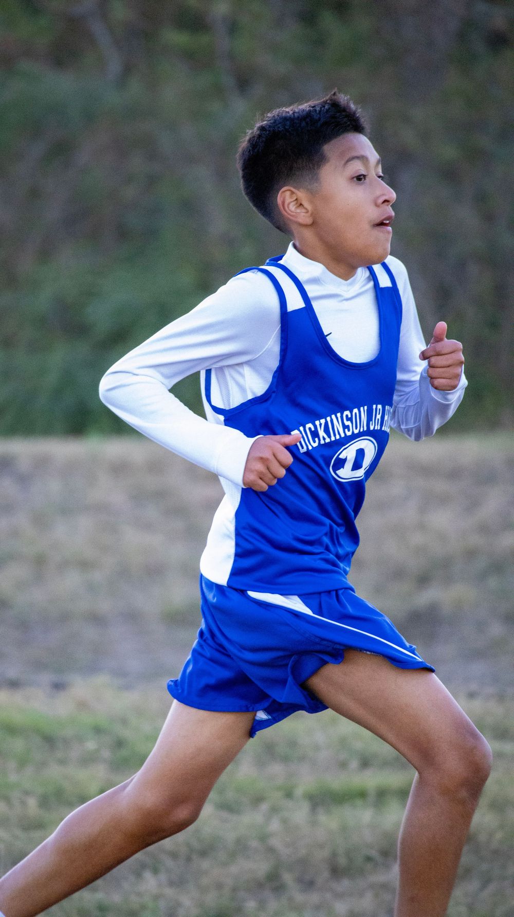 Athlete in blue and white uniform demonstrating running form on grass field.