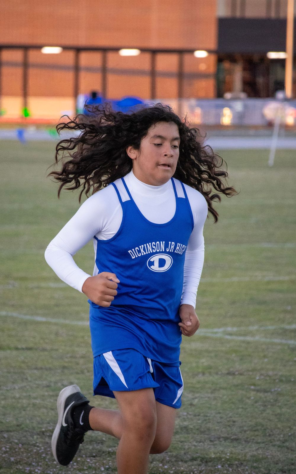 Runner in blue and white uniform sprinting across sports field with hair flowing.