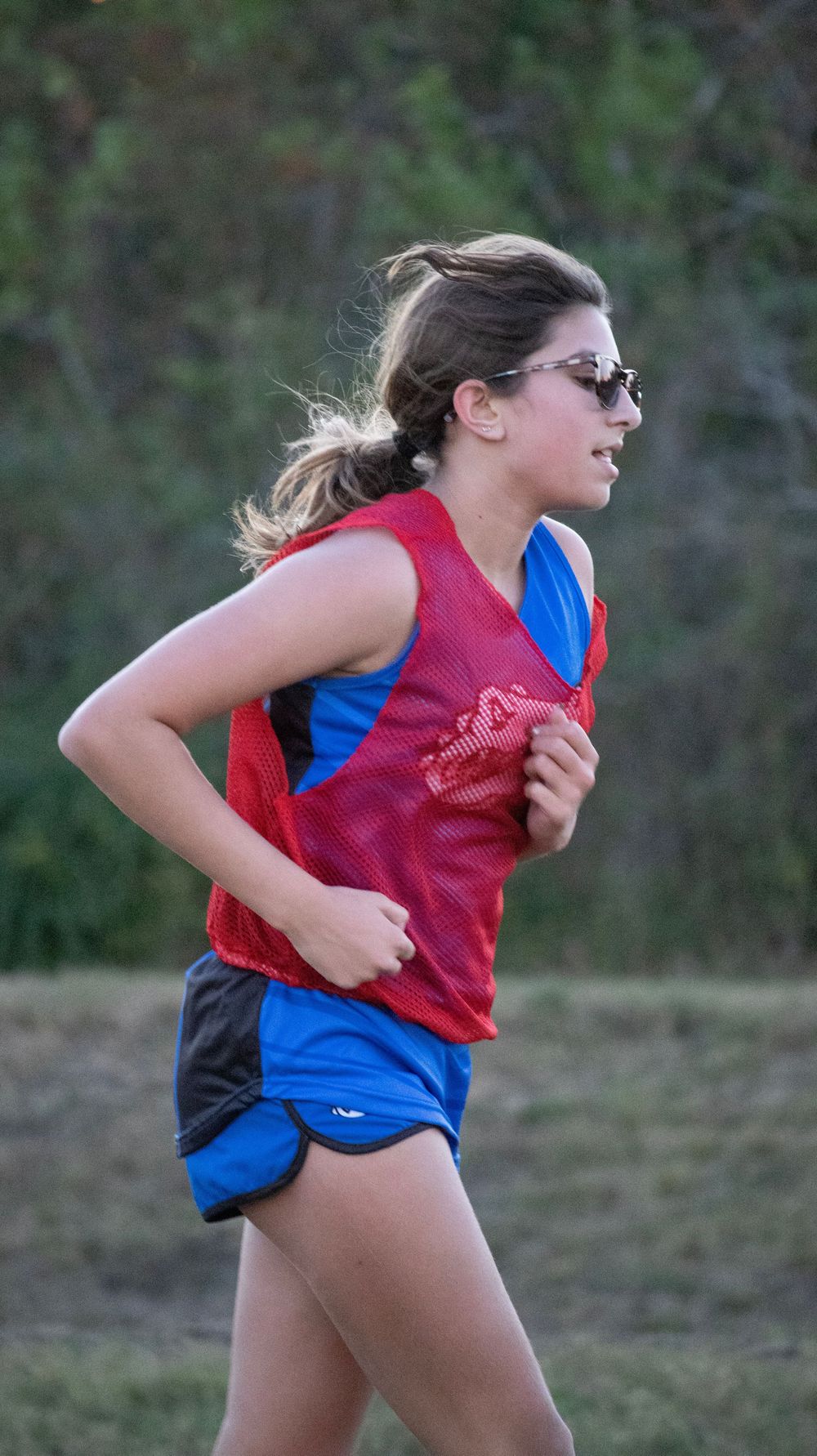 Runner in red and blue uniform practicing sprints on outdoor field.