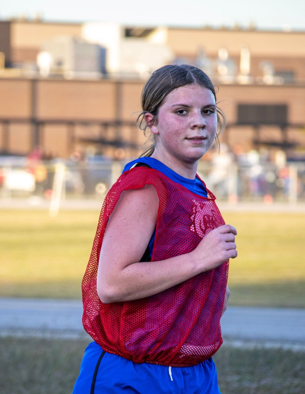Young athlete in red and blue sports uniform running on a field during practice.