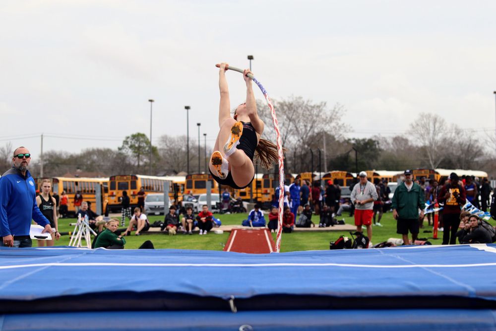 Track and field athletes prepare for long jump competition at an outdoor stadium.