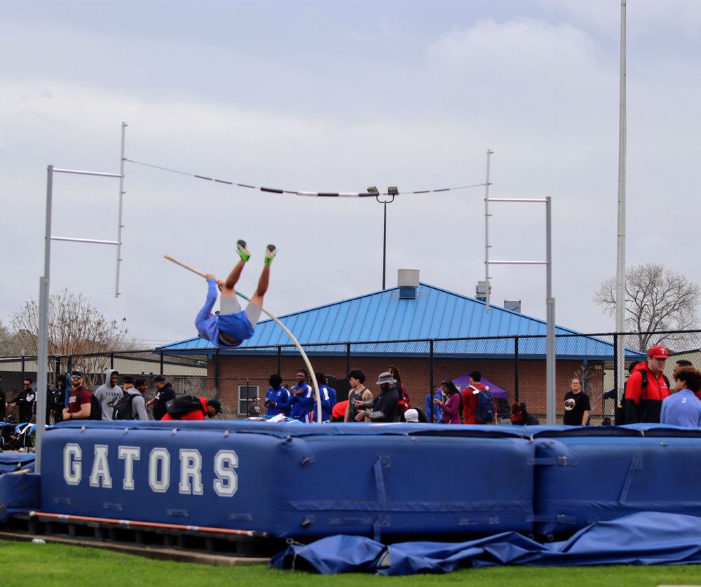 Track athlete executes pole vault technique against cloudy sky at Gators athletic facility.