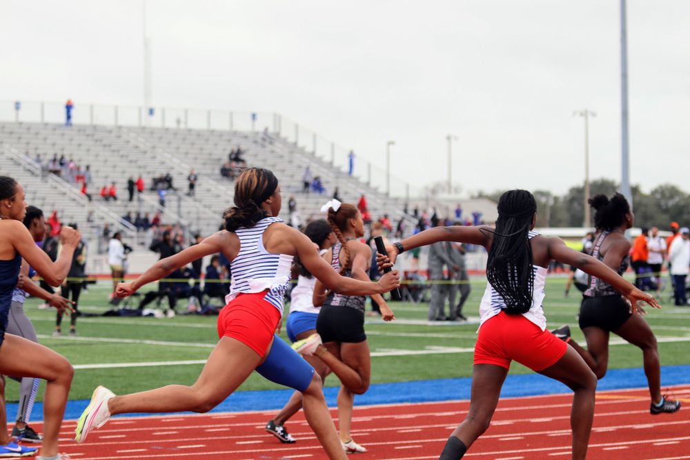 Track athletes stretch in formation on red track during pre-meet warmup.