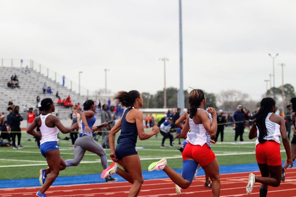 Athletes perform dynamic stretches in a row on red track surface during warmup routine.