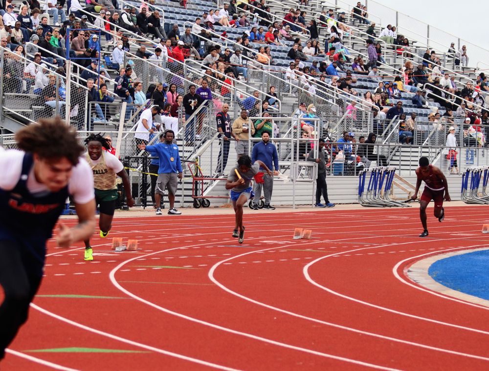 Sprinters competing in a track race with spectators watching from stadium bleachers.