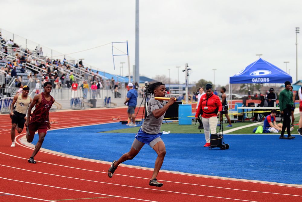 Competitive sprinters racing on an outdoor track with spectators watching from the stands.