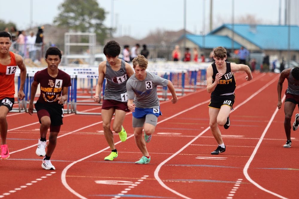 Athletes competing in a sprint race on a red track during a sunny day competition.