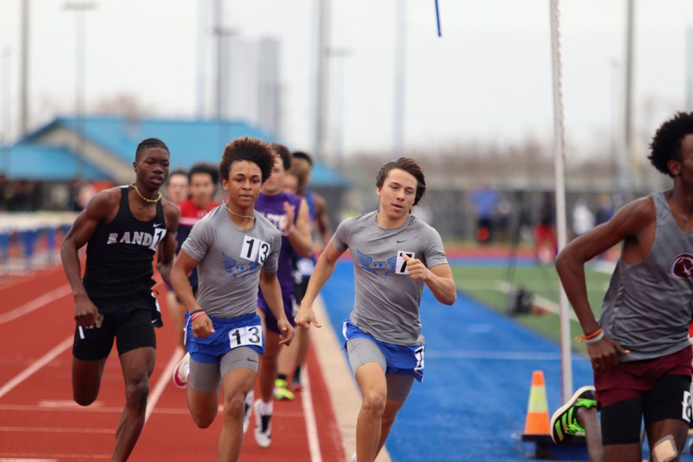Sprinters competing in a close race on a red track during an outdoor meet.