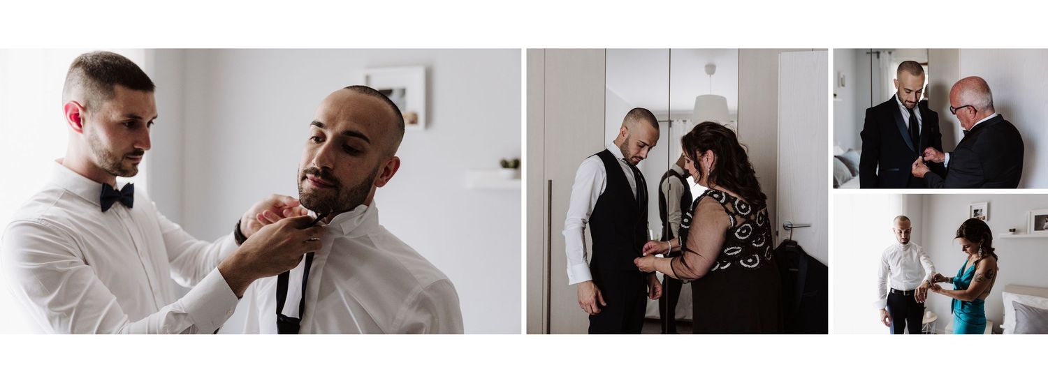 Groom getting tie adjusted by groomsman while family assists with final wedding preparations indoors.