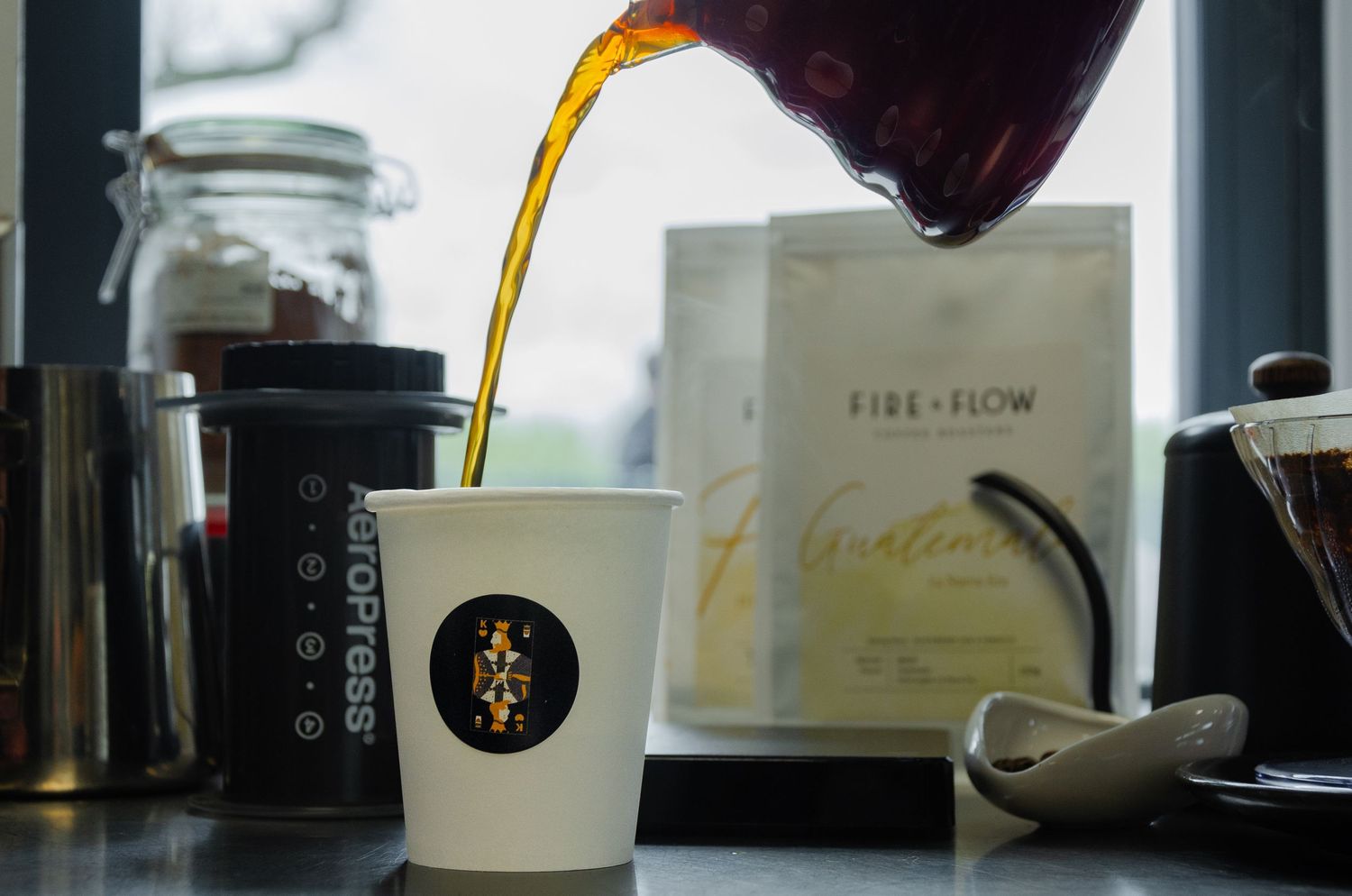 A white paper cup with hand-drawn artwork is held up to display the design.