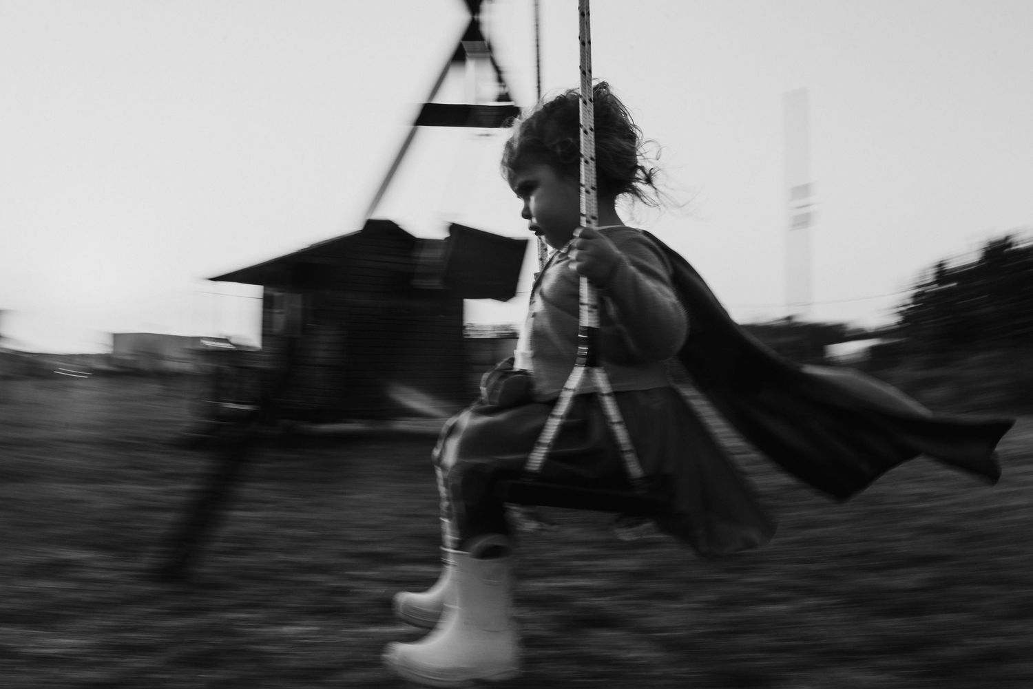 Niña en movimiento hamacándose con disfraz de superhéroe. Foto documental en blanco y negro.