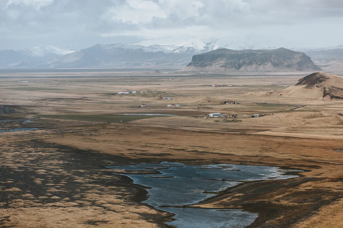 Dramatic aerial view of a black sand beach coastline with mountains and small settlements in the distance.
