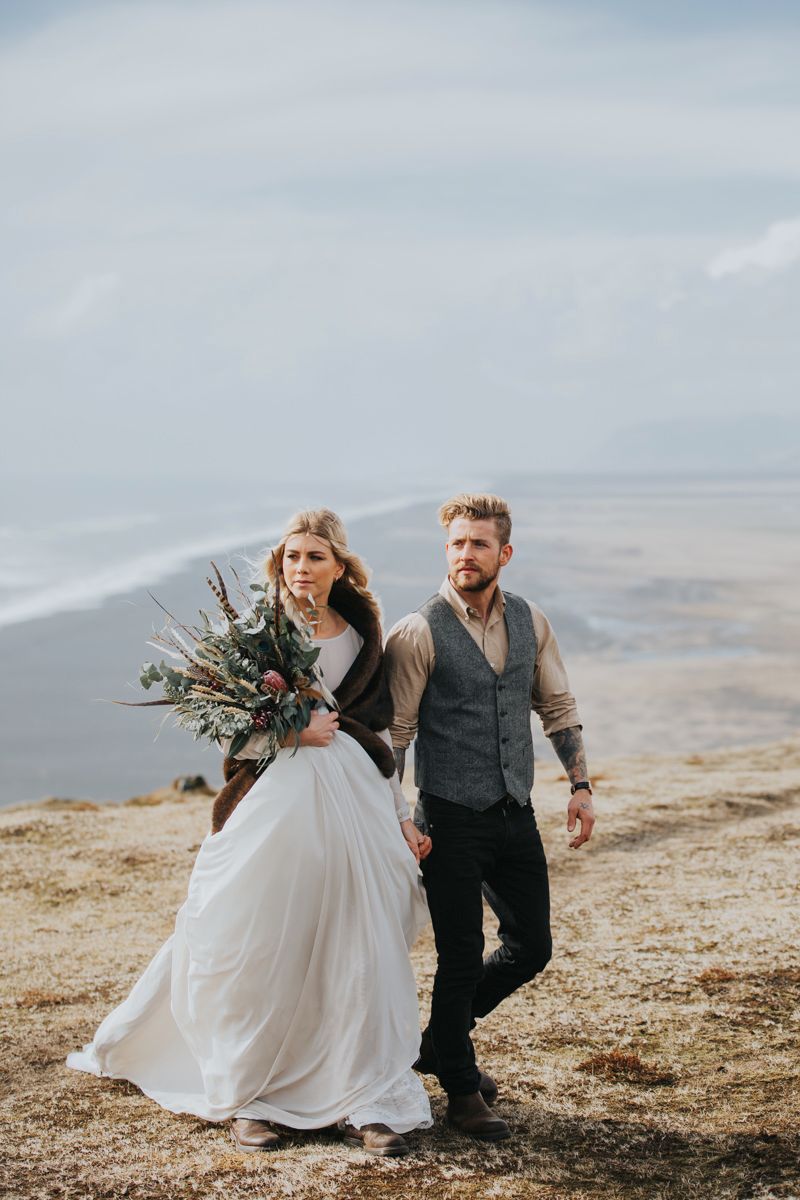A coastal wedding photoshoot featuring flowing white dress and rustic attire against dramatic cliffside scenery.