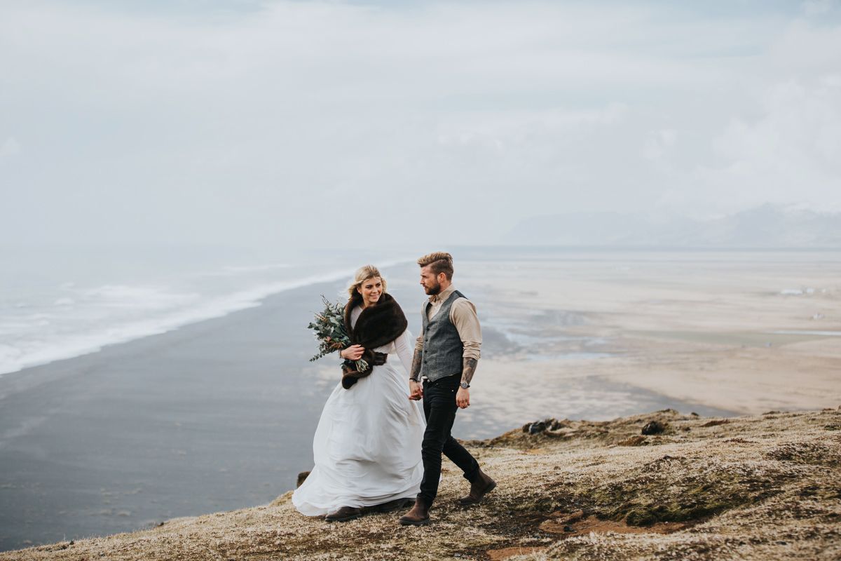Wedding couple walking along dramatic coastal cliffs with sweeping ocean views.