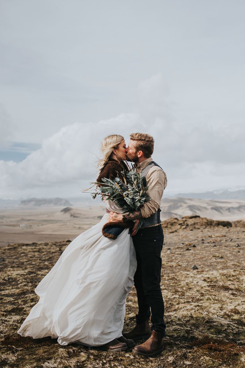 Intimate wedding moment captured on windswept cliffs with dramatic landscape views.