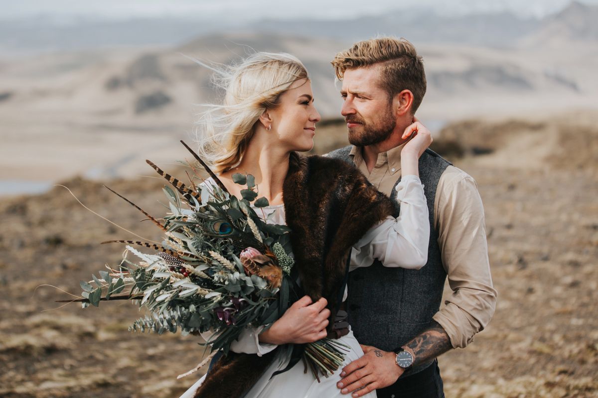 Romantic wedding portrait with rustic bouquet against moody mountain landscape.