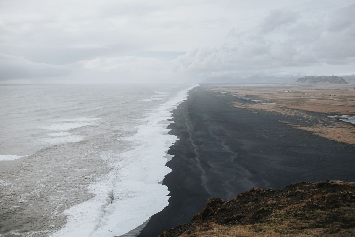 Dramatic black sand beach meets ocean waves along Iceland's rugged volcanic coastline.