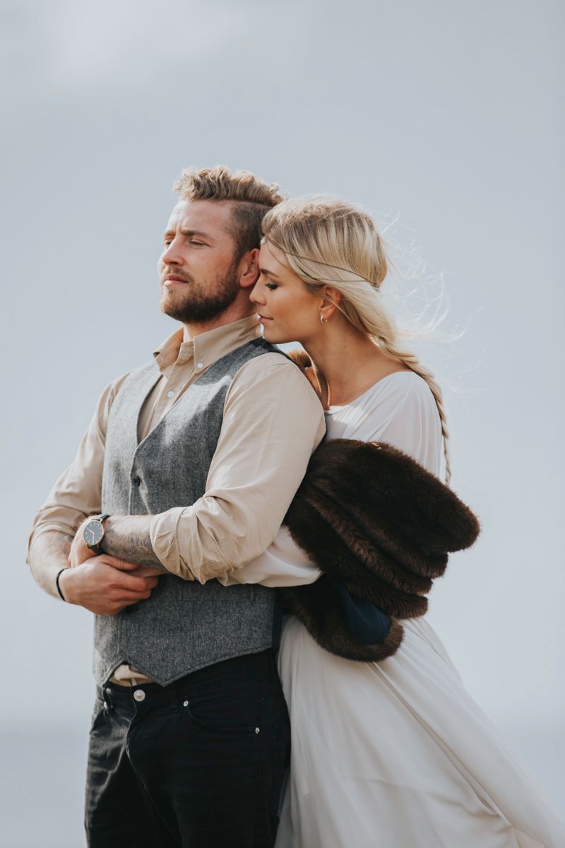 Artistic wedding photo capturing tender moment between couple on windswept cliff.