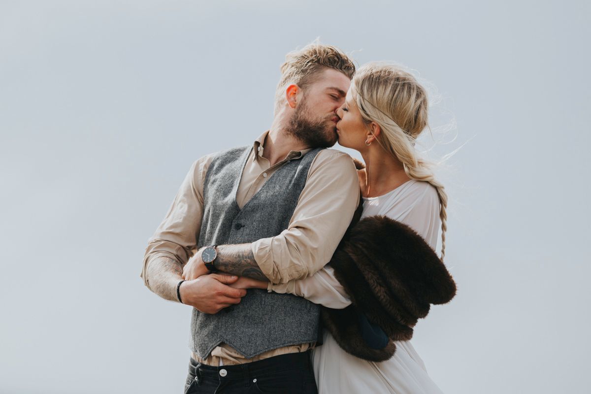 Romantic wedding couple shares intimate moment on dramatic coastal backdrop.