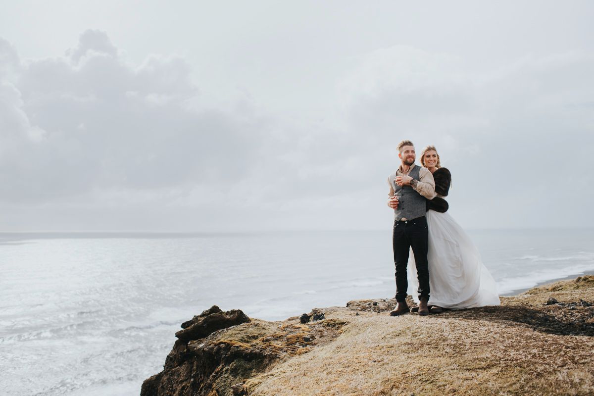 Intimate wedding portrait showing couple embracing on dramatic coastal cliffside.