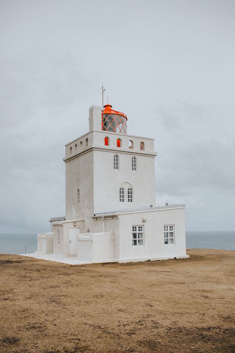 White lighthouse tower with orange top stands alone on barren landscape under cloudy sky.