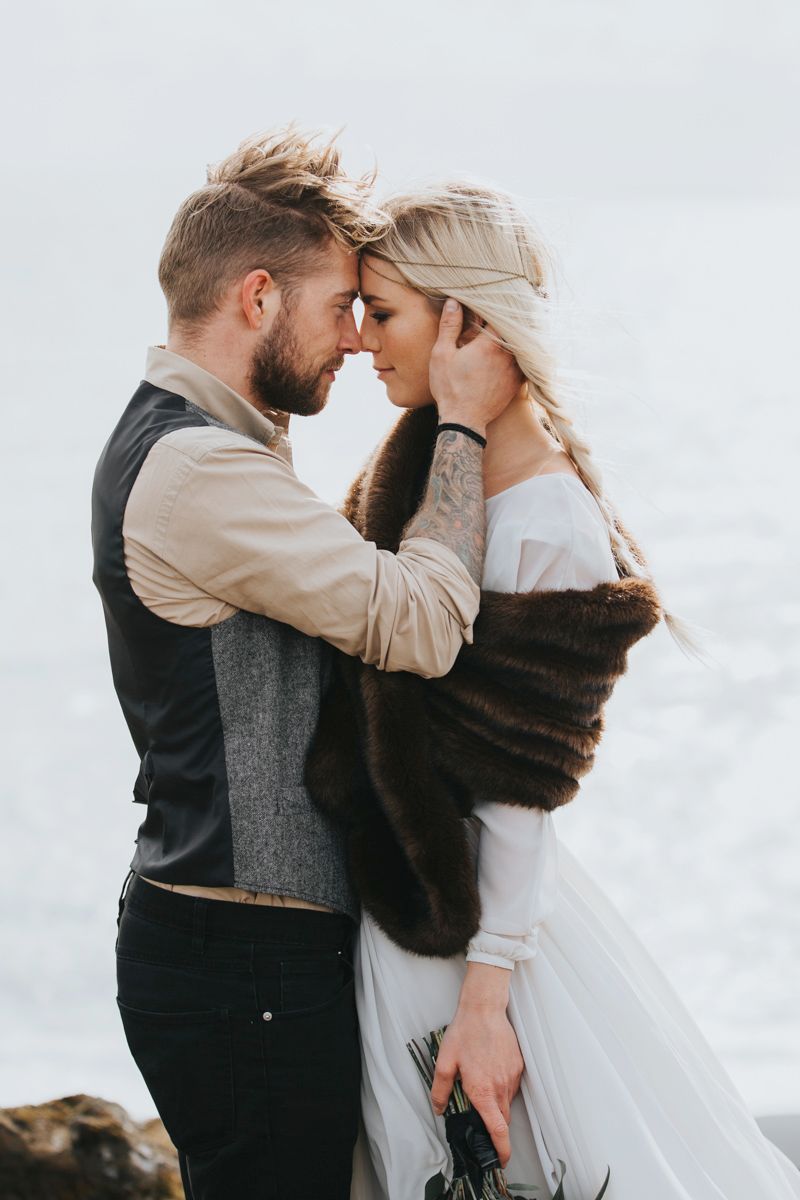 Intimate wedding portrait of couple embracing on windswept coastal cliffs.