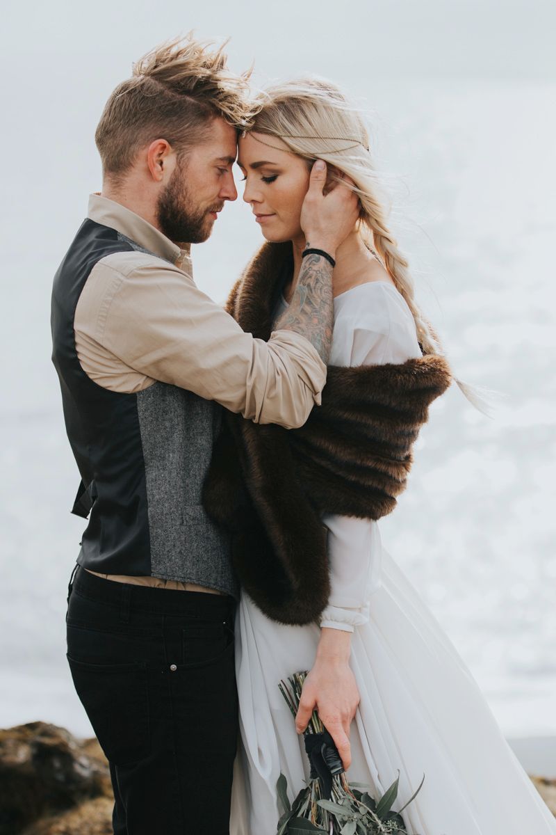 Romantic wedding photo of couple sharing tender moment against cloudy backdrop.