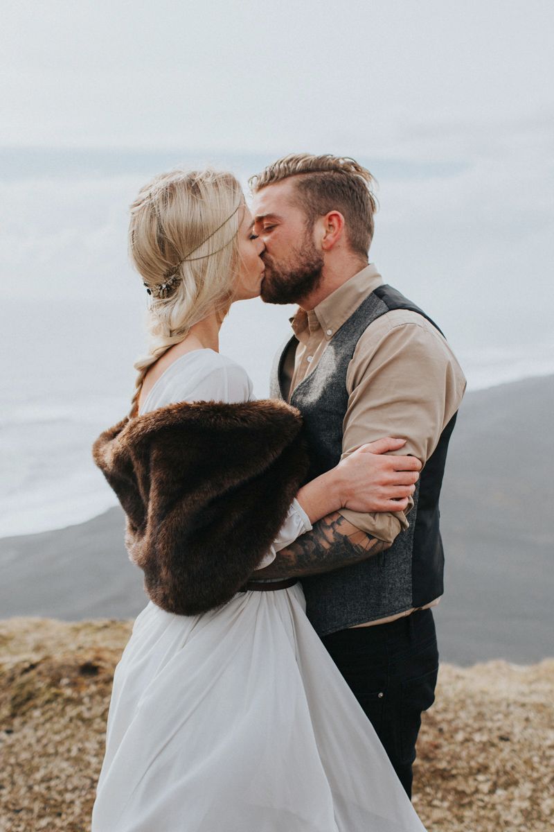 Wedding couple sharing kiss on dramatic coastal overlook.