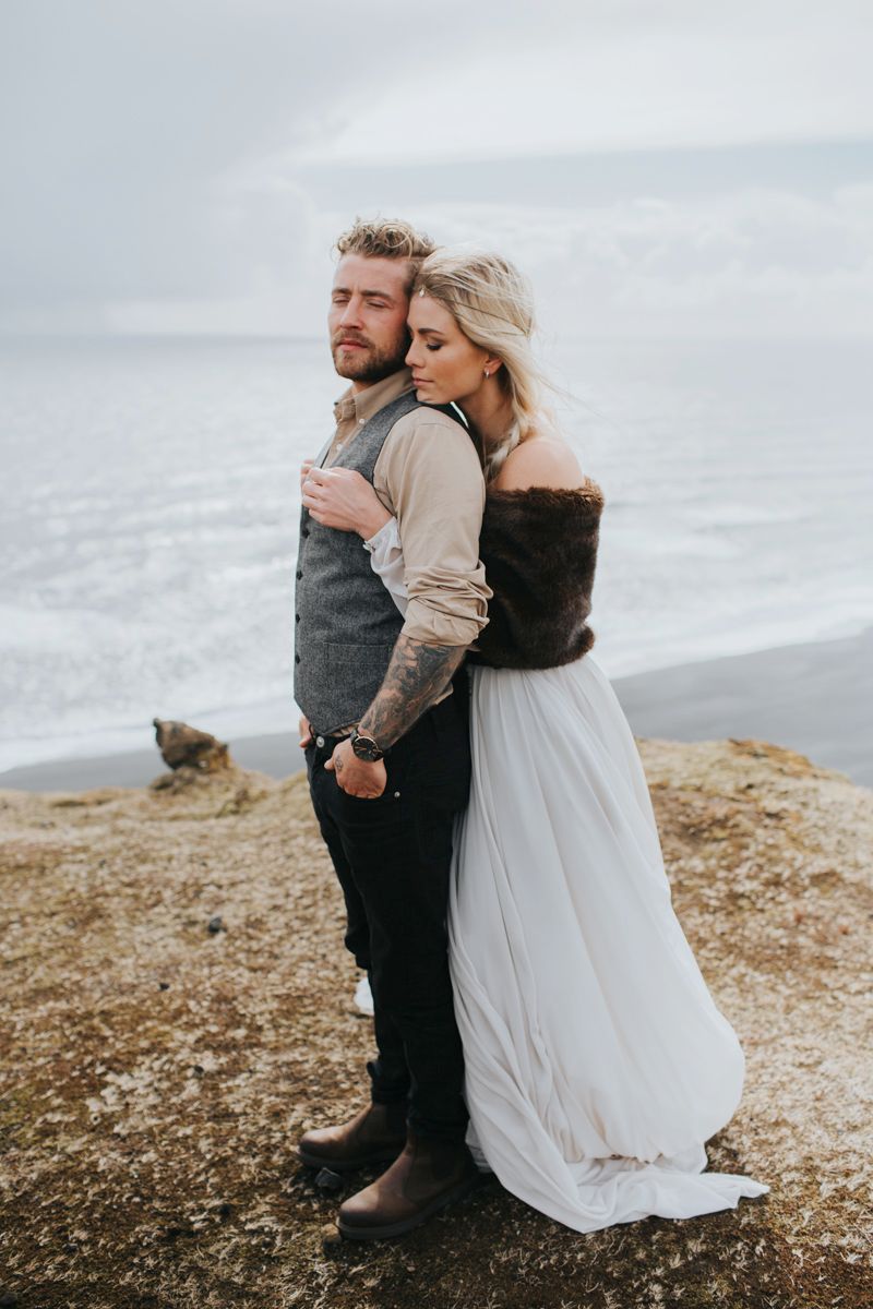 Stylish wedding couple embracing on rugged coastal cliff edge.