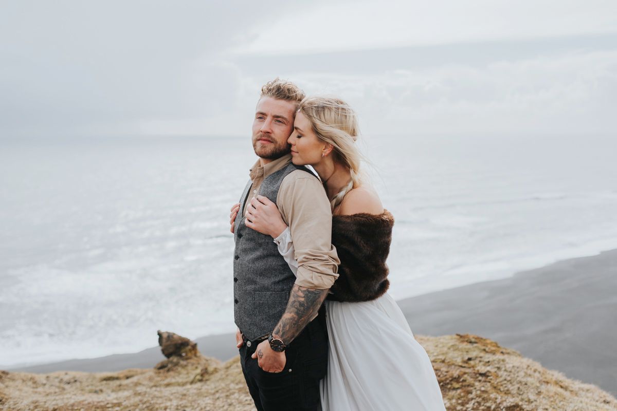 A romantic wedding couple embraces on a clifftop overlooking a misty ocean view.