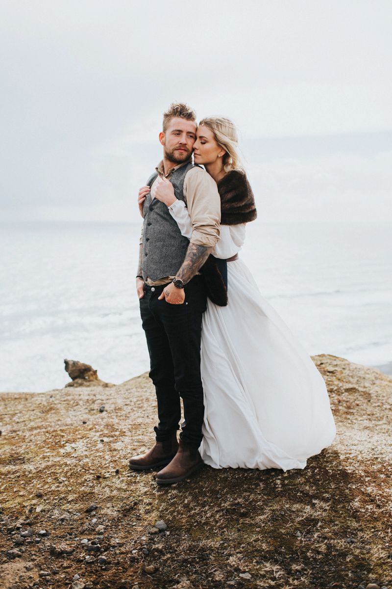 Newlyweds share an intimate moment on a coastal cliff edge during their wedding photoshoot.