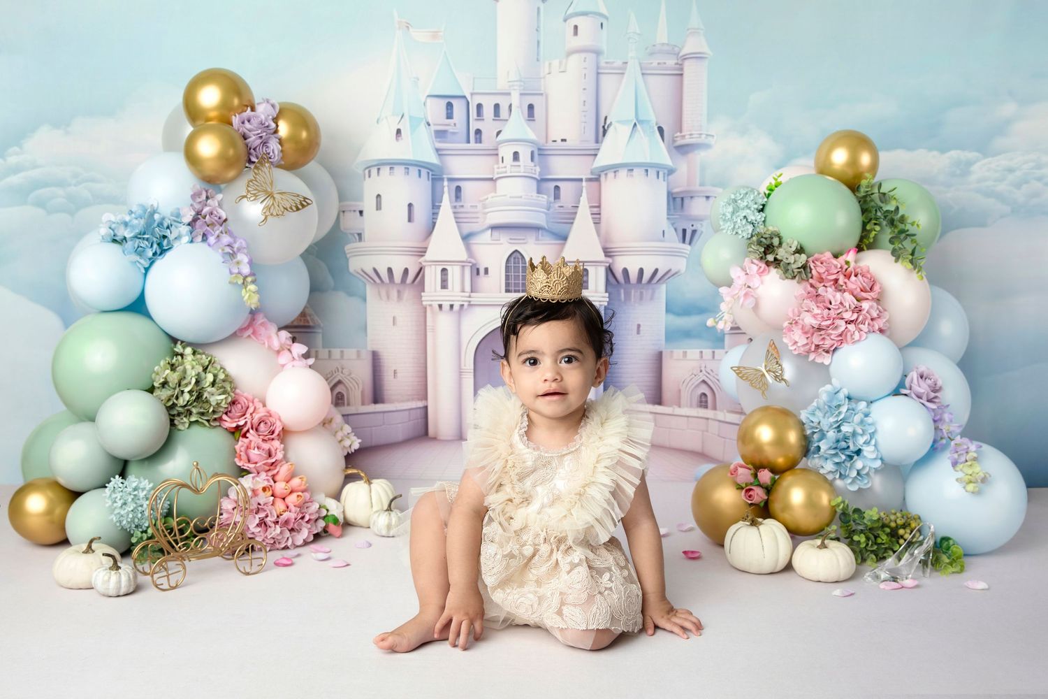 Fantasy castle backdrop with pastel balloon arch and floral decorations for baby photography.