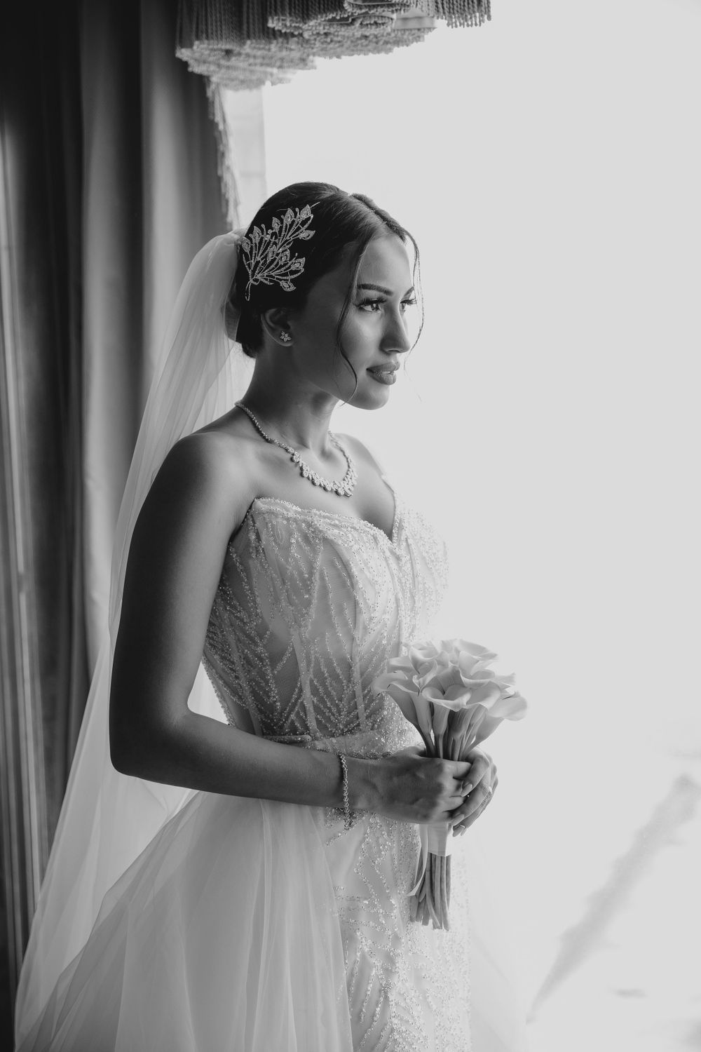 Classic black and white portrait of bride by window holding bouquet.