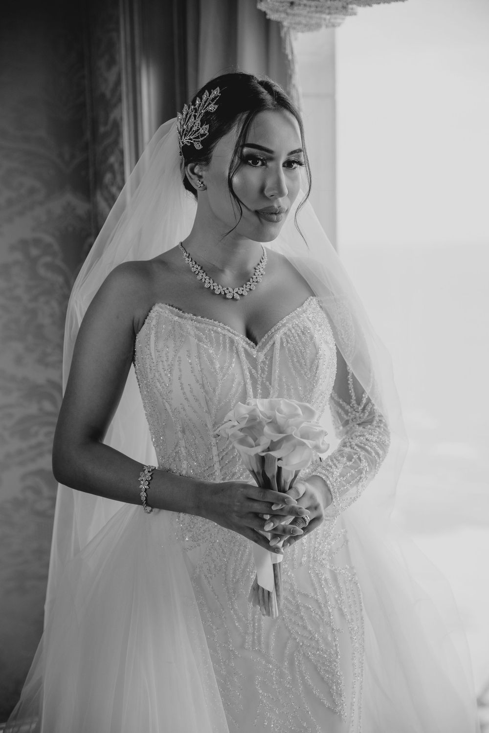 Black and white photo of bride wearing crystal accessories and holding white flowers.
